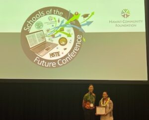 Michelle Aquino receives the 2025 Hawai'i History Teacher of the Year award from HCH Board Member Kristen Namba Reed on stage at the Schools of the Future conference.