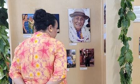A woman looks at a display of photos of kumu hula draped with lei.